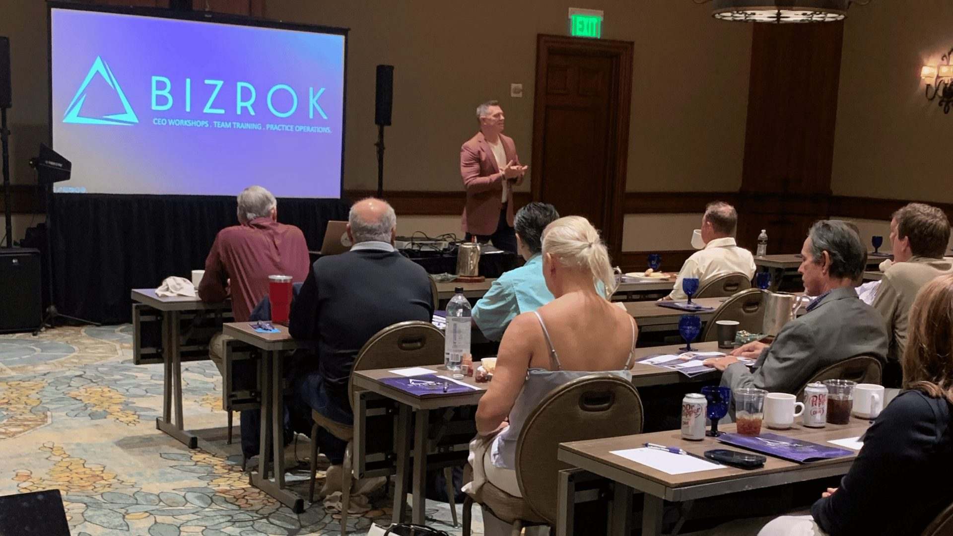 BIZROK branded screen at a seminar with attendees seated at tables